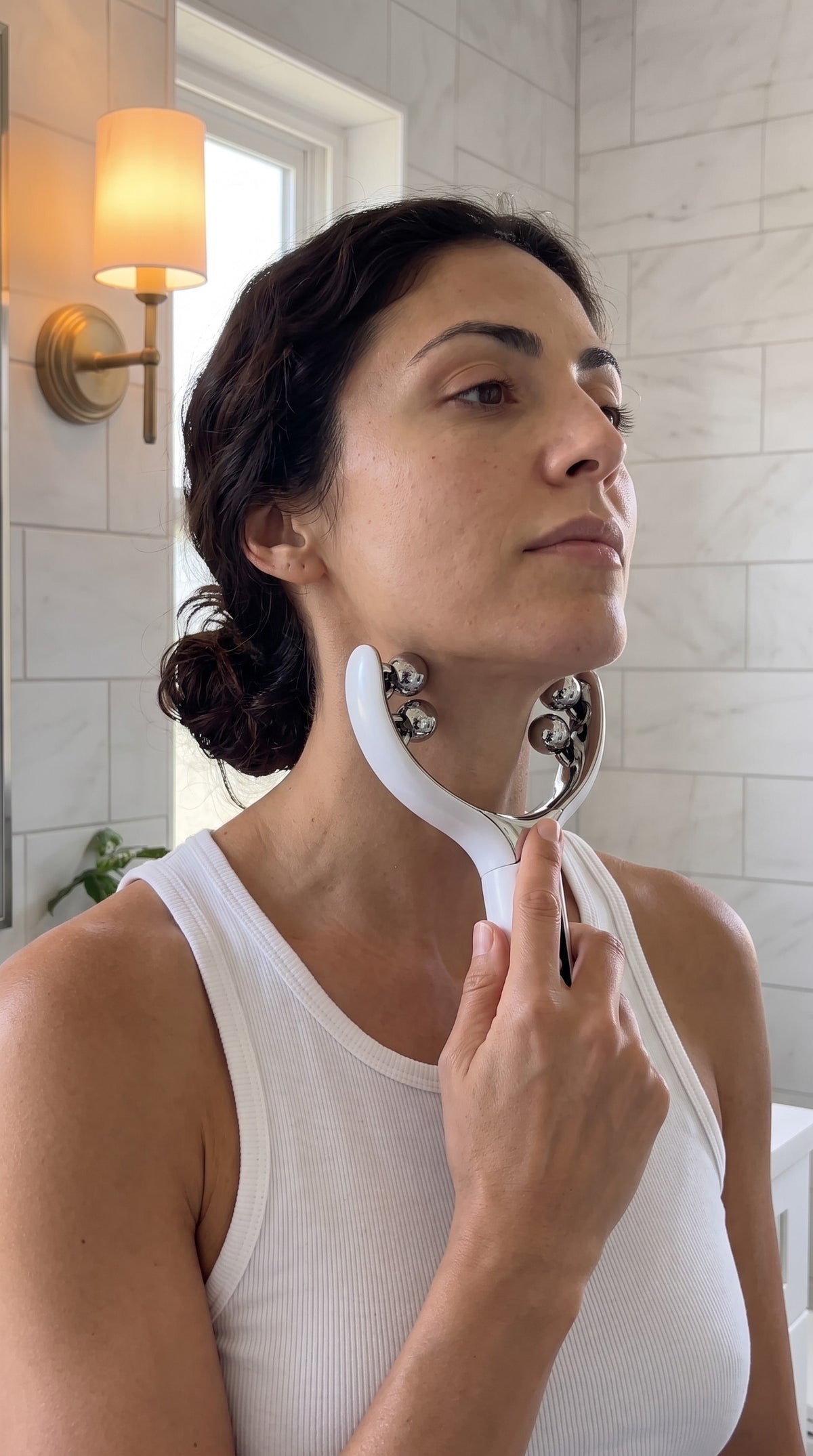Woman gliding the 8-roller facial massager along the neck