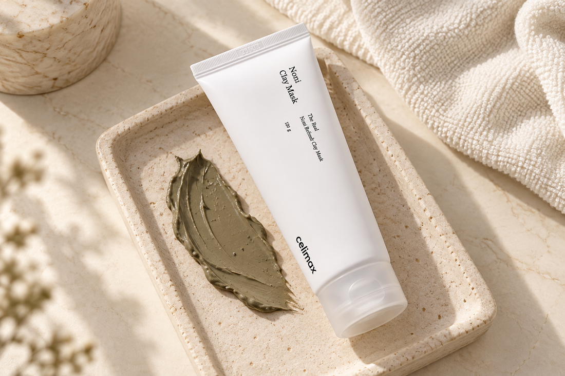Celimax Noni Clay Mask tube beside a clay smear and washcloth on a warm ivory vanity