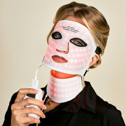 Woman wearing wireless 7-color LED photon light therapy face and neck mask, soft studio lighting