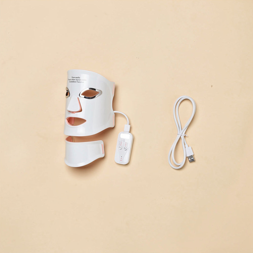 Wireless LED light therapy face and neck mask kit: mask, charging cable, and controller neatly arranged, soft studio lighting