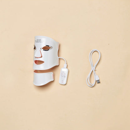Wireless LED light therapy face and neck mask kit: mask, charging cable, and controller neatly arranged, soft studio lighting