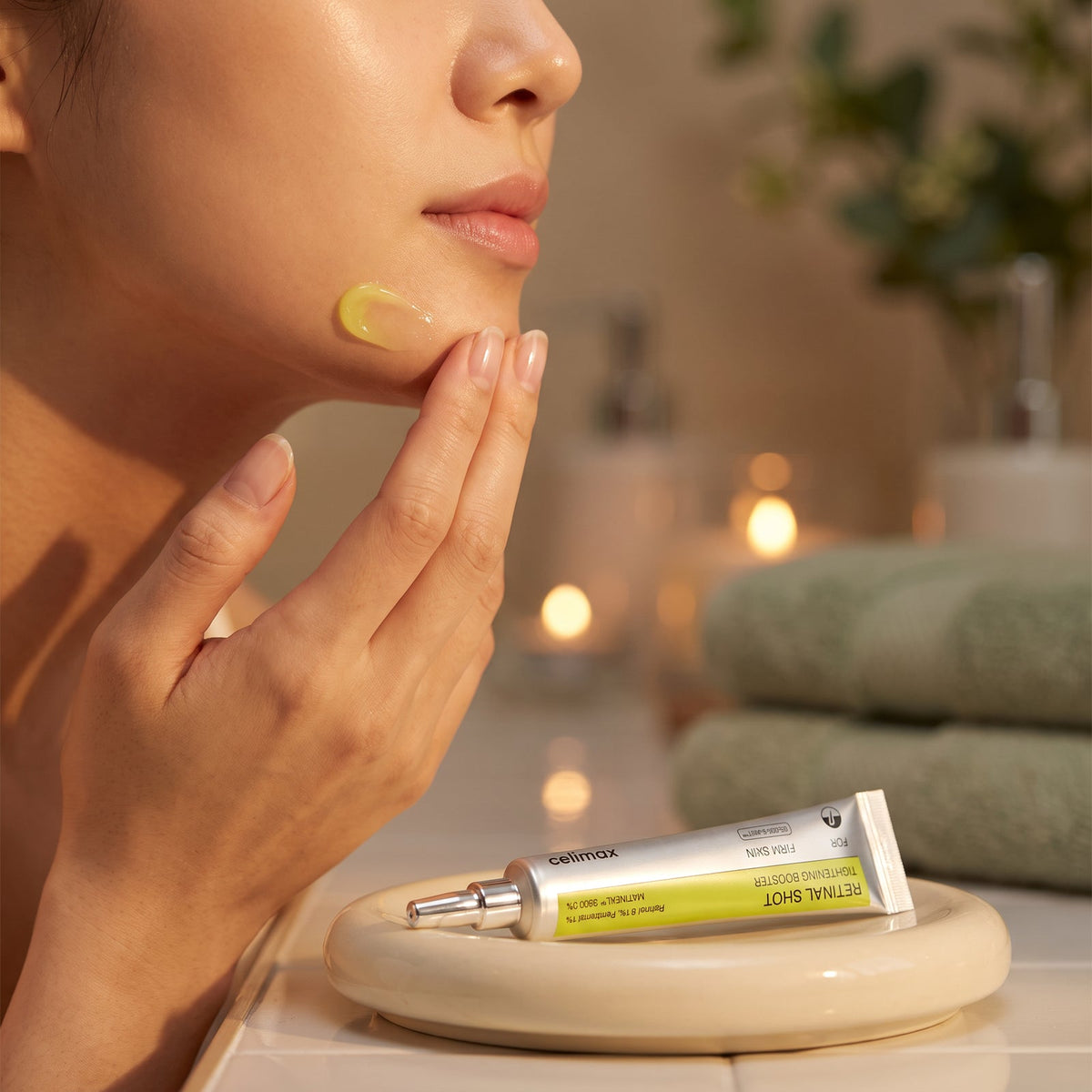 Celimax Vita-A Retinal Shot Tightening Booster tube beside a hand applying gel serum to the jawline in warm evening light