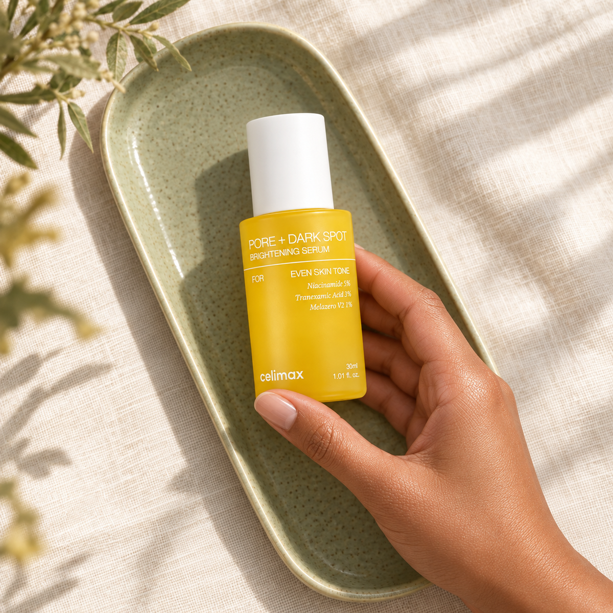 A hand holding Celimax Brightening Serum 30 mL on a sage ceramic tray