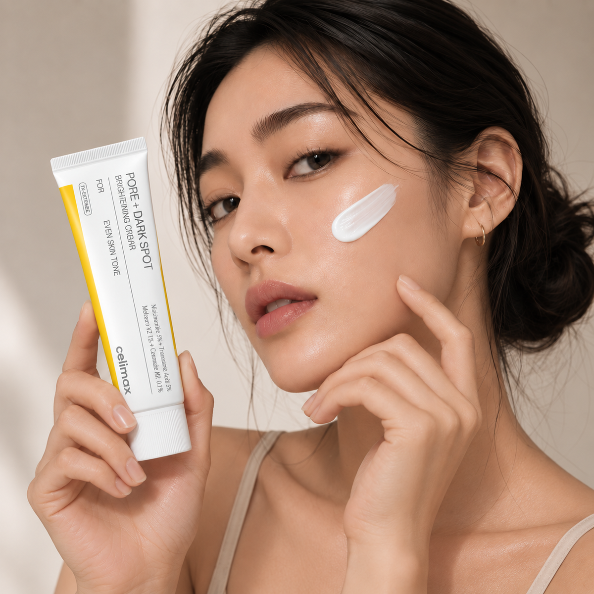 Woman holding Celimax Pore + Dark Spot Brightening Cream with a cream swatch on her cheek