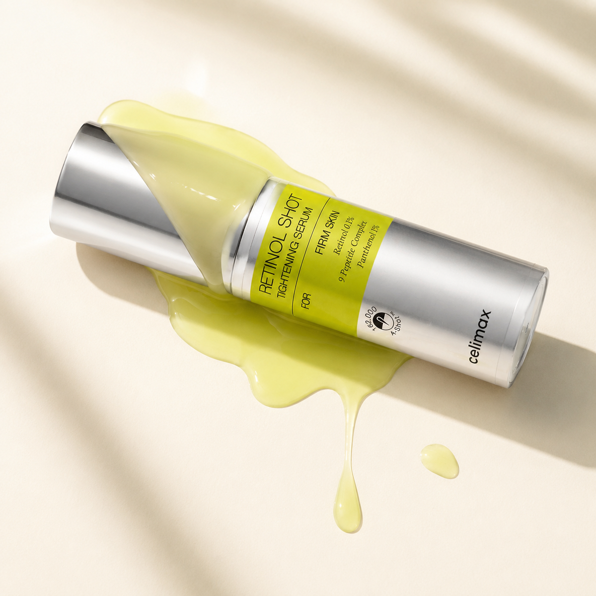 Celimax Retinol Shot Tightening Serum bottle tipped on its side with yellow-green gel dripping onto a cream background