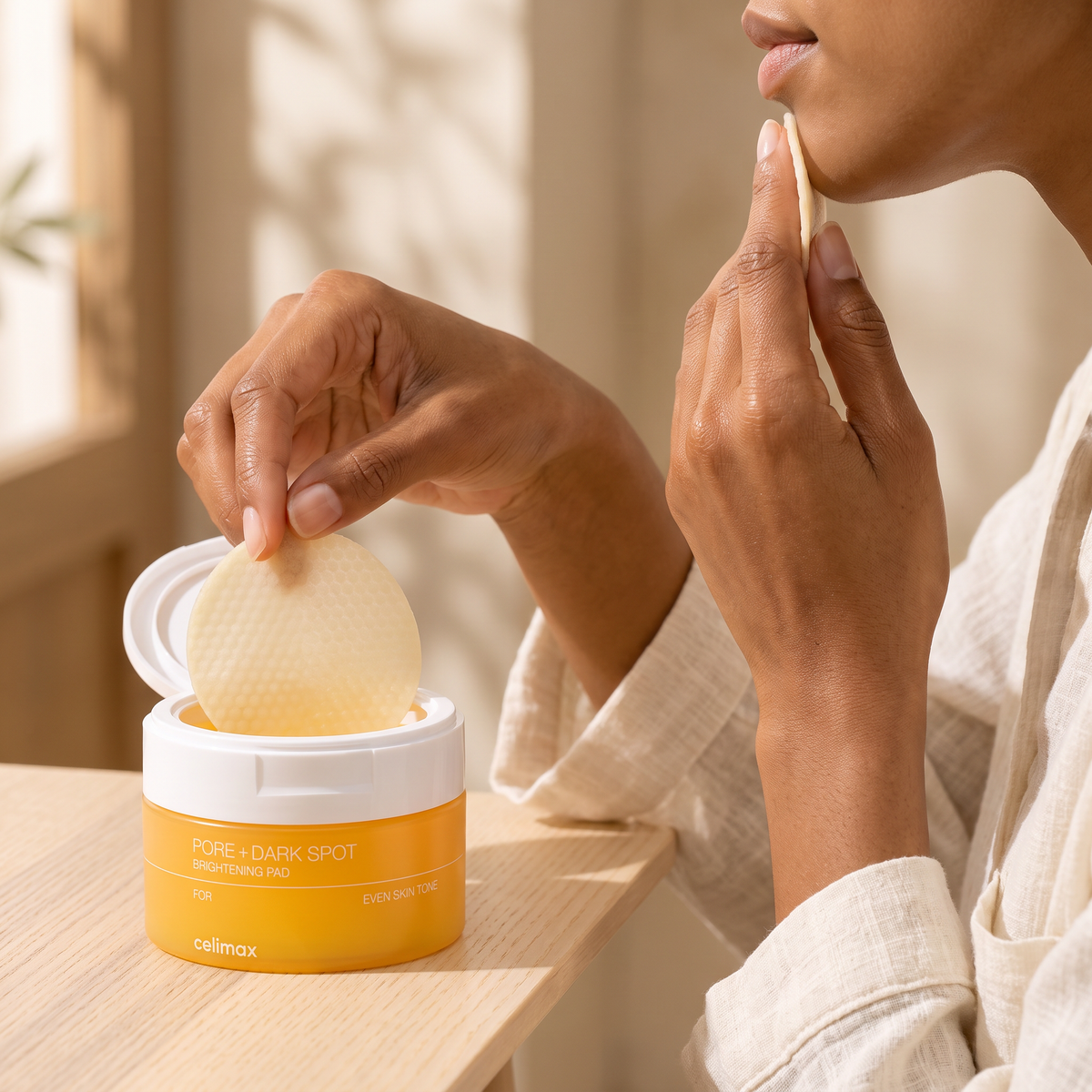 Hands applying a Celimax Pore + Dark Spot Brightening Pad along the jawline